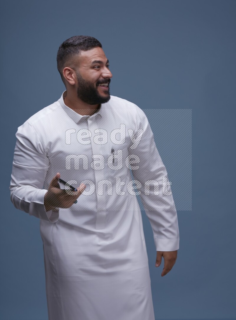 A man Showing his phone in Blue Background wearing Saudi Thob