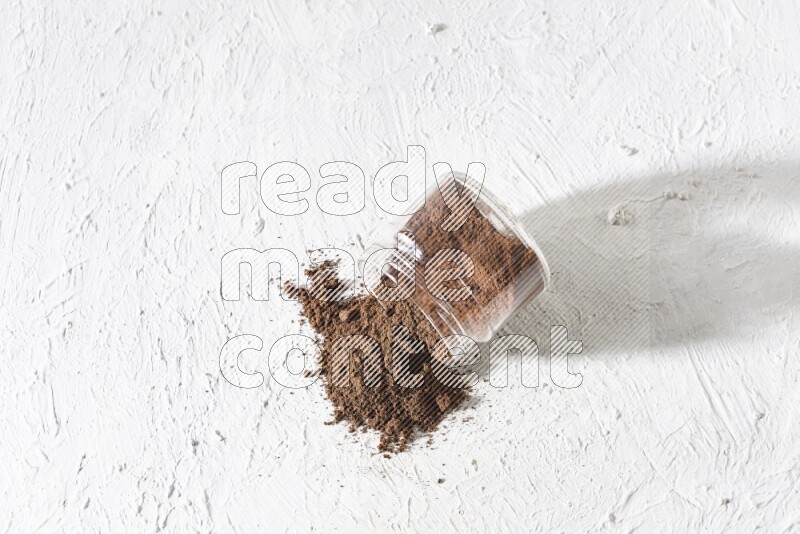 A flipped glass jar full of cloves powder on a textured white flooring