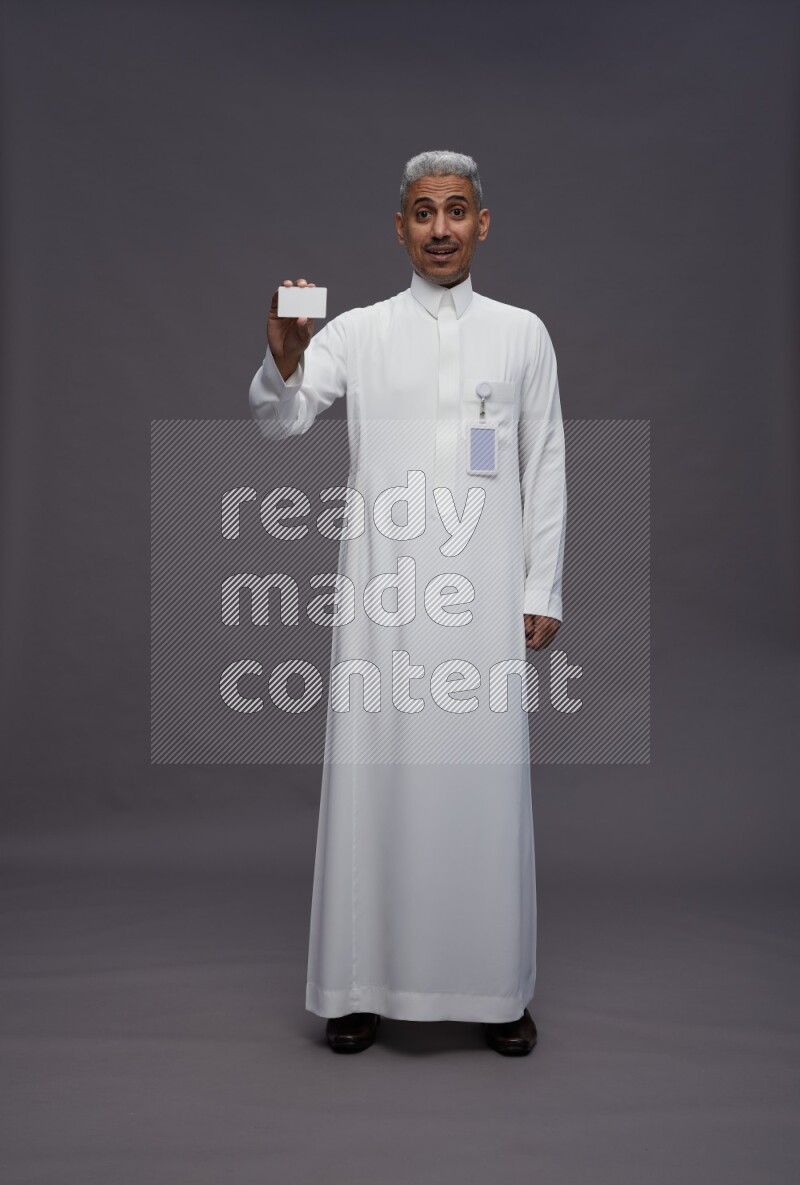 Saudi man wearing thob with pocket employee badge standing holding ATM card on gray background