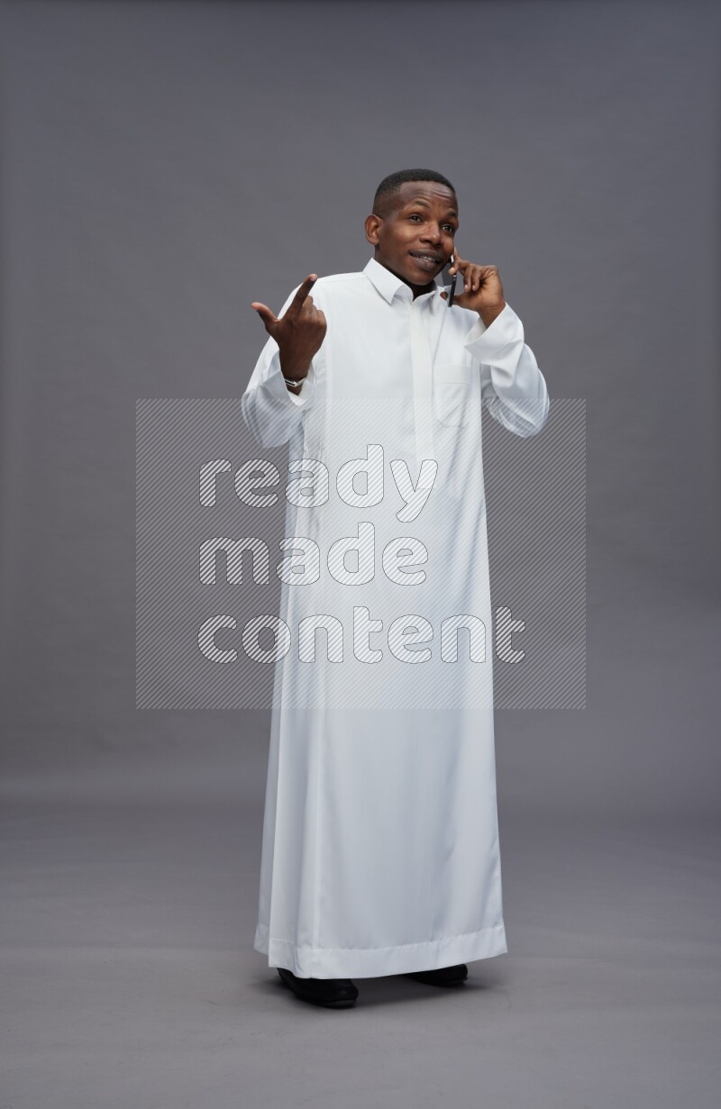 Saudi man wearing thob standing talking on phone on gray background