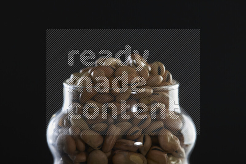 Fava beans in a glass jar on black background