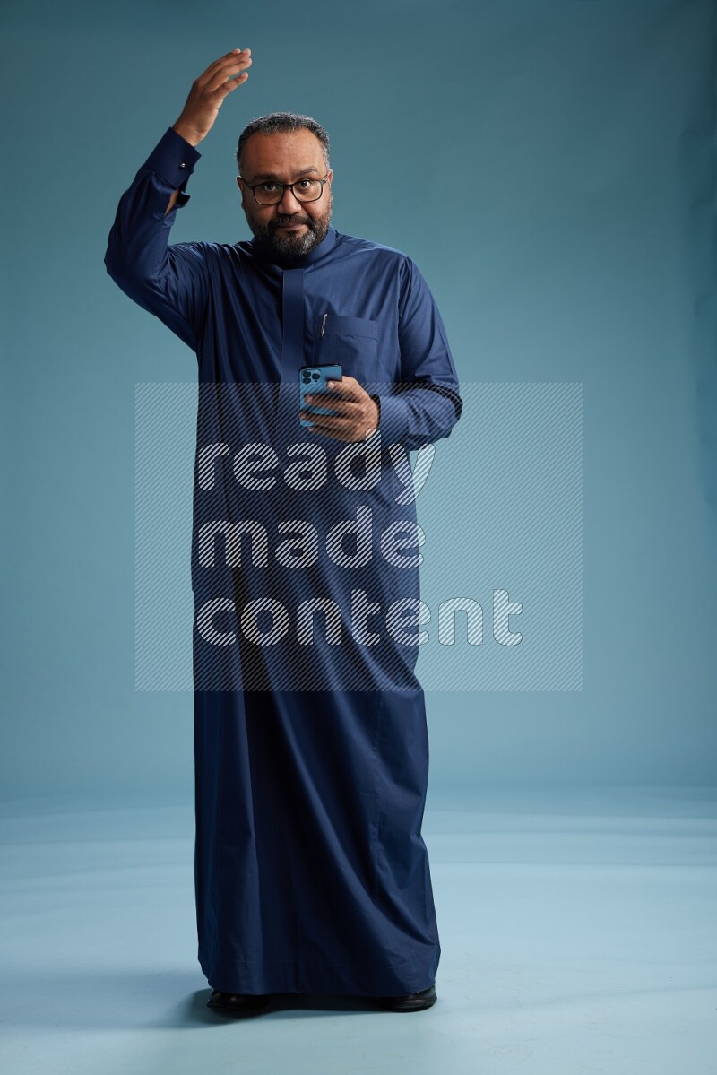 Saudi Man without shimag Standing texting on phone on blue background