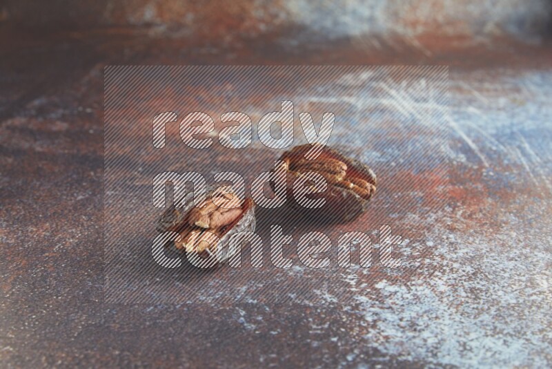two pecan stuffed madjoul dates on a rustic reddish background