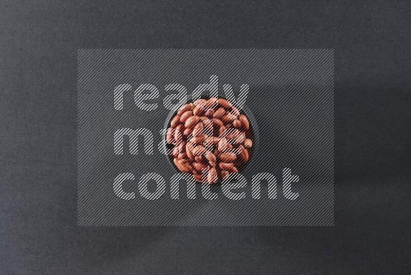 A black pottery bowl full of red skin peanuts on a black background in different angles