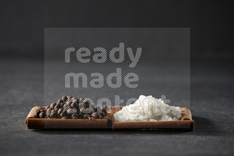 مربعان من أعواد القرفة ممتلئان بالملح الأبيض وحبوب الفلفل الحلو علي خلفية سوداء