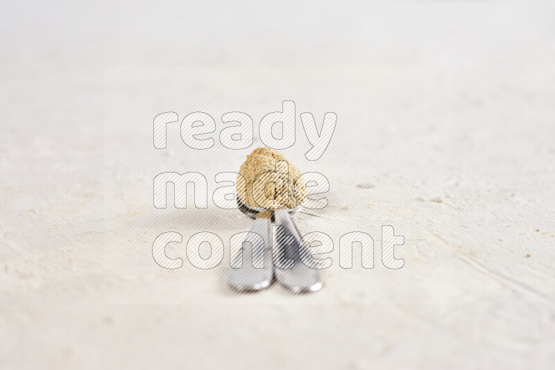 Two metal spoons full of ground ginger powder on white background