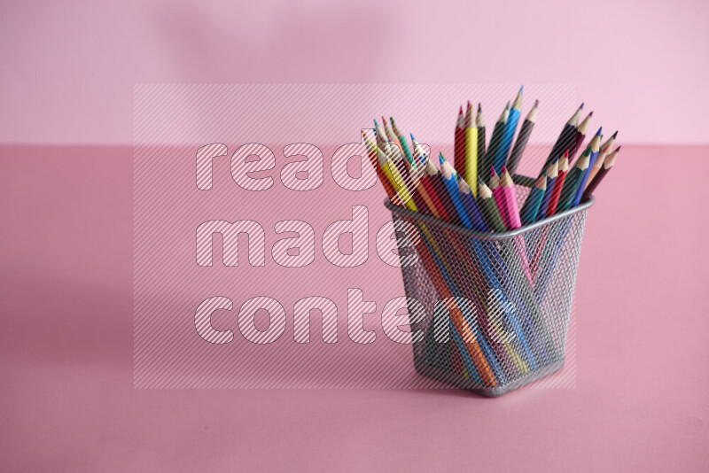 Pens, pencils and other different school supplies in a metal pen holder on rose background