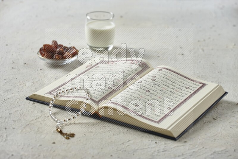 Quran with dates, prayer beads and different drinks all placed on textured white background