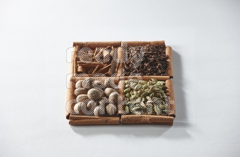 4 مربعات من أعواد القرفة ممتلئة بالهيل والقرفة والقرنفل وجوزة الطيب على أرضية بيضاء