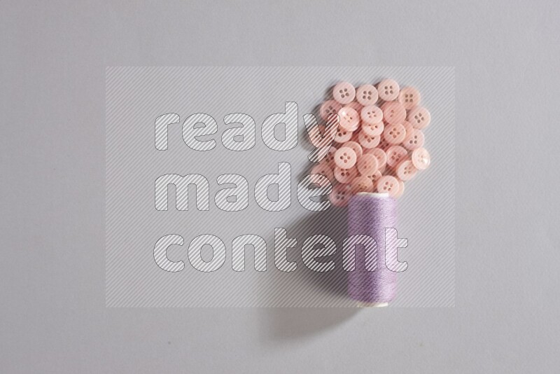 A purple sewing thread spool with small bunch of buttons on grey background