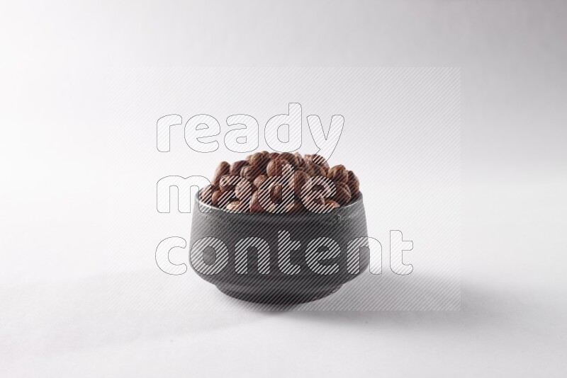 Hazelnuts in a black pottery bowl on white background