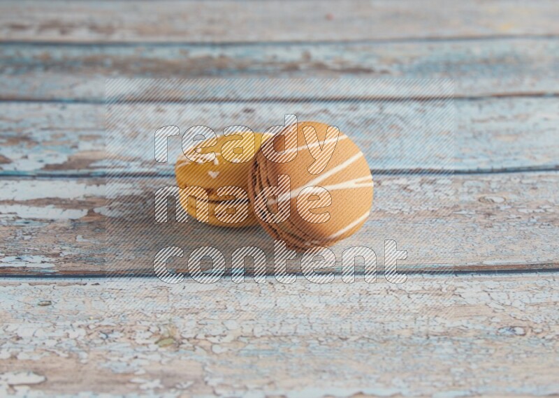 45º Shot of of two assorted Brown Irish Cream, and Yellow Piña Colada macarons on light blue background