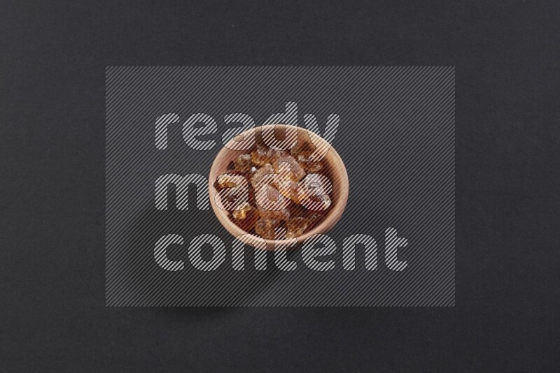 A wooden bowl full of gum arabic on a black flooring