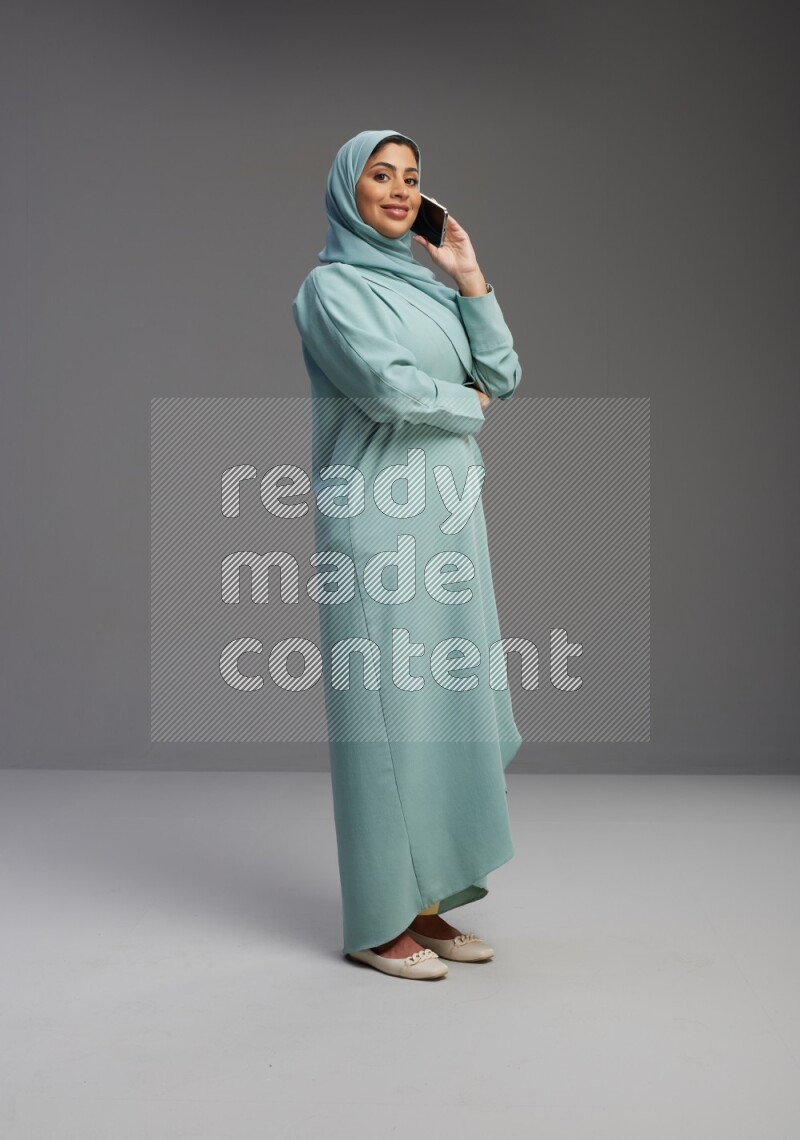 Saudi Woman wearing Abaya standing talking on phone on Gray background