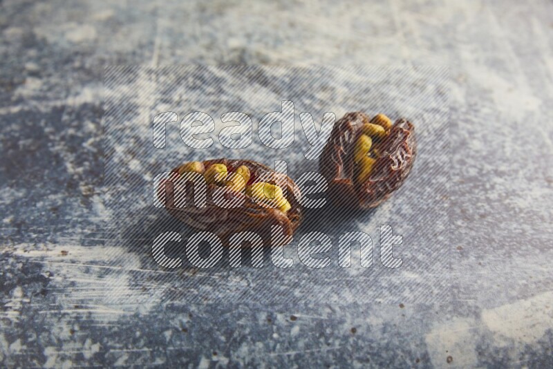 two pistachios stuffed madjoul dates on a rustic blue background