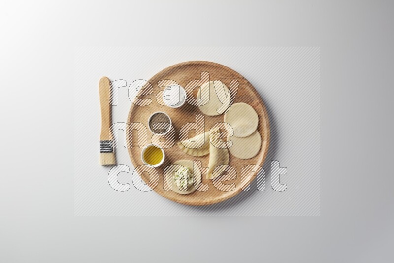 two closed sambosas and one open sambosa filled with cheese while salt, black pepper and oil with oil brush aside in a wooden dish on a white background