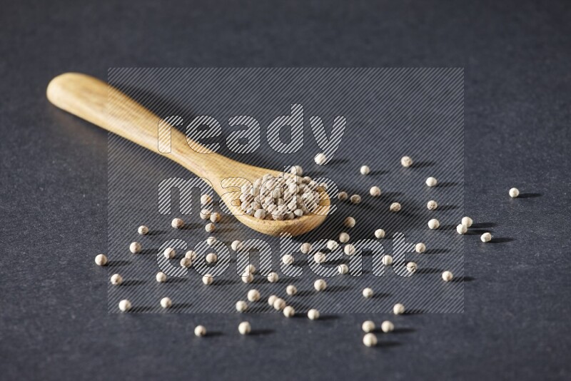 A wooden spoon full of white pepper beads on black flooring