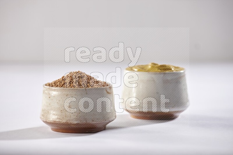 2 beige pottery bowls full of mustard seeds and mustard paste on white flooring in different angles