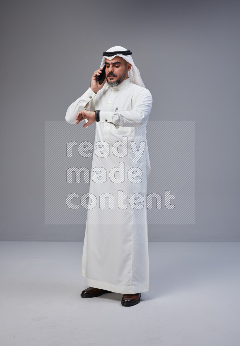 Saudi man Wearing Thob and white Shomag standing talking on phone on Gray background