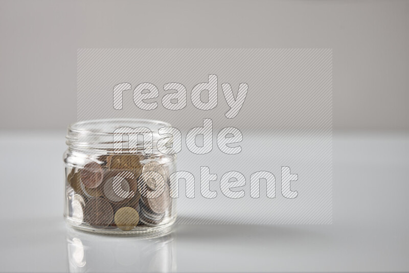 Random old coins in a glass jar on grey background