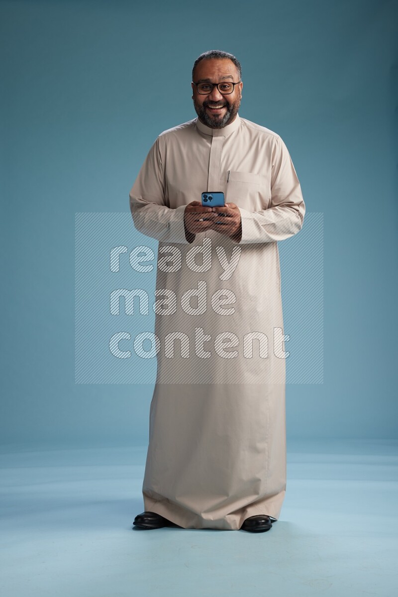 Saudi Man without shimag Standing texting on phone on blue background
