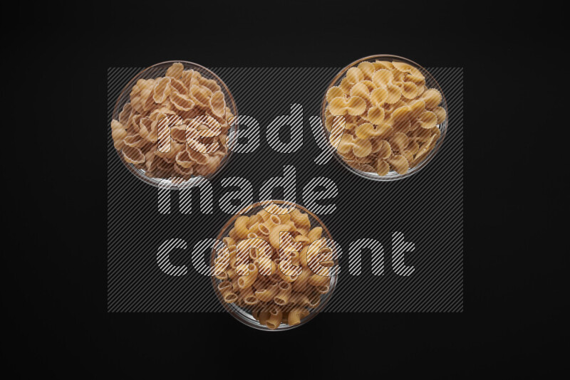 Different pasta types in glass bowls on black background