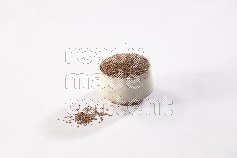 A pottery beige bowl full of flax seeds and more seeds spread on a white flooring