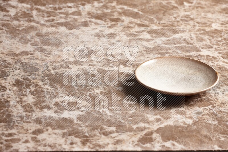 A beige pottery plate on beige marble background