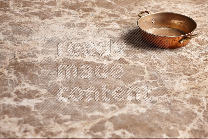 A small copper pan on beige marble background