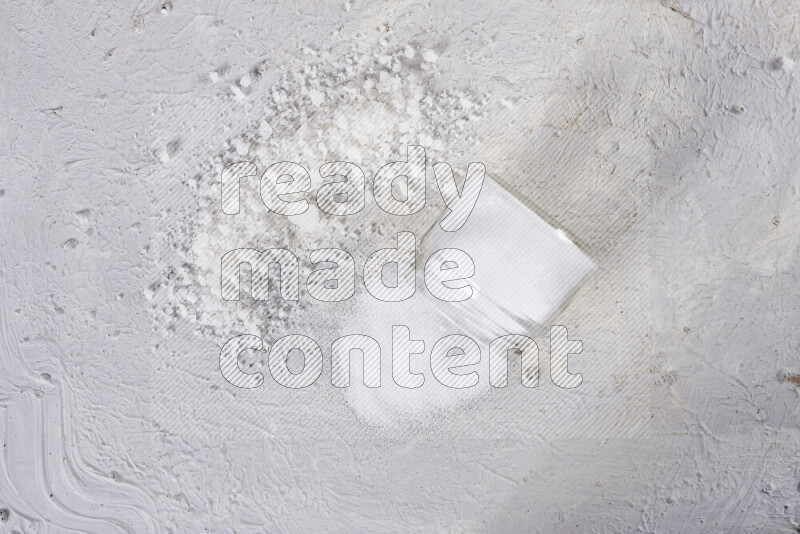 A glass jar full of table salt with some sea salt crystals beside it on a white background