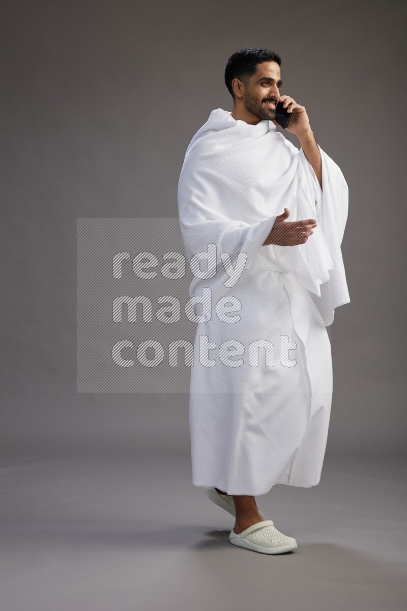 A man wearing Ehram Standing talking on phone on gray background