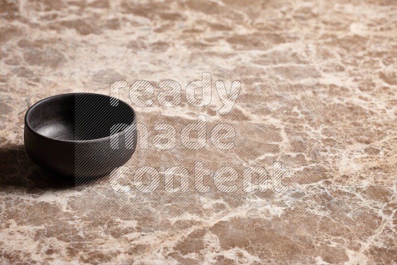 A black pottery bowl on beige marble background