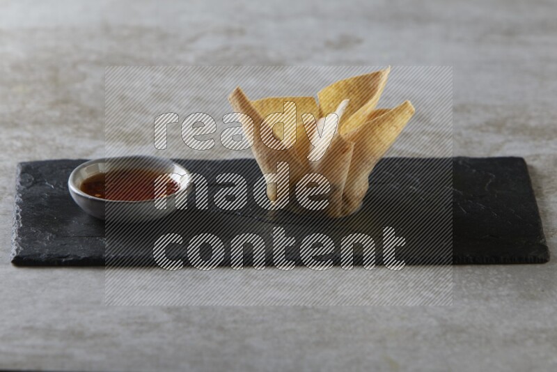 wonton cups with soy sauce ramkin on rectangle slate on grey textured counter top