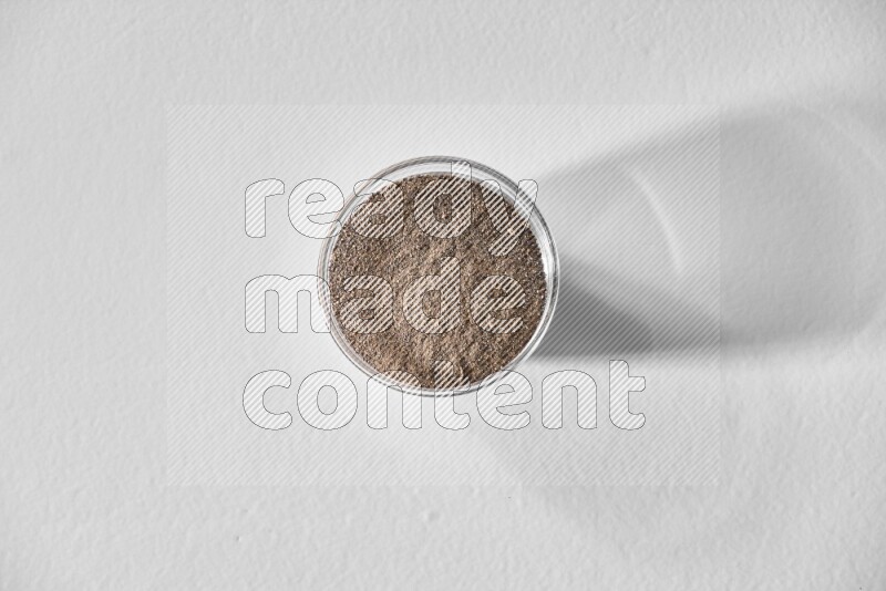 A glass bowl full of black pepper powder on white flooring
