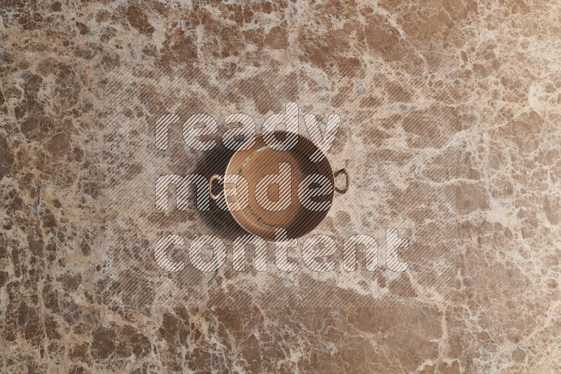 A small copper pan on beige marble background