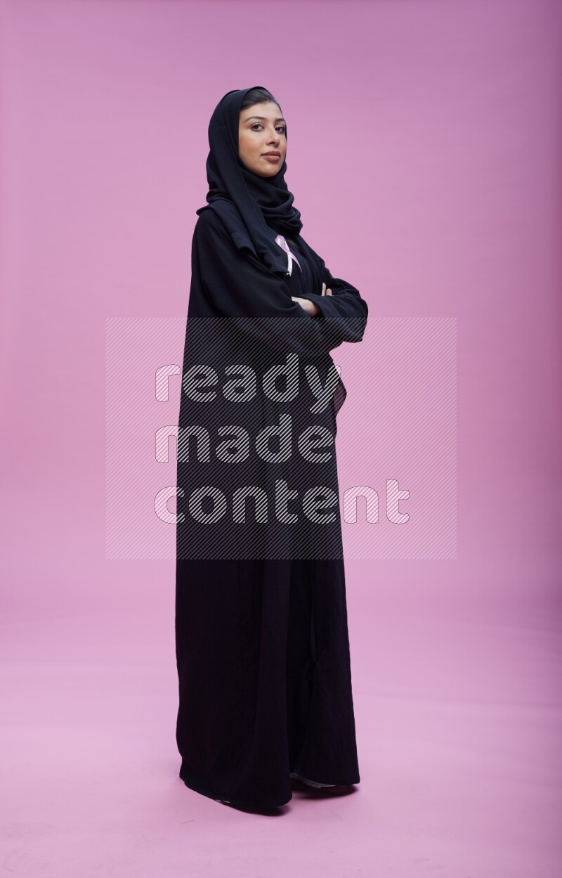 Saudi woman wearing Abaya standing with crossed arms on pink background