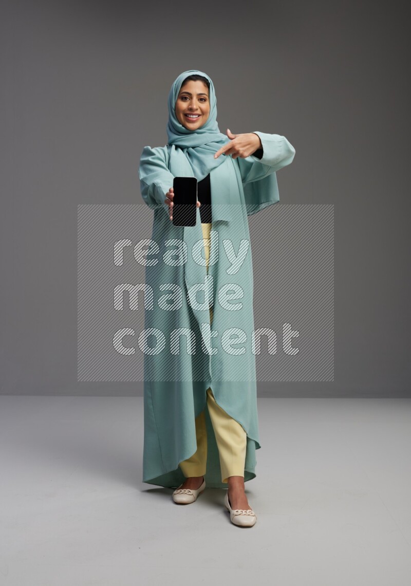 Saudi Woman wearing Abaya standing showing phone to camera on Gray background