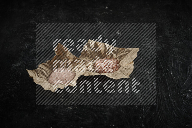 A crumpled piece of paper full of pink himalayan salt on black background