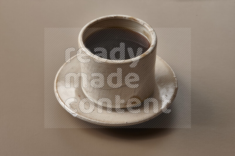 A beige pottery cup of coffee surrounded by roasted coffee beans on beige background