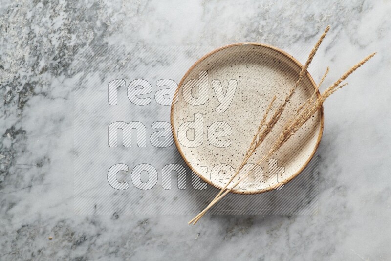 Wheat stalks on multicolored pottery plate on grey marble background
