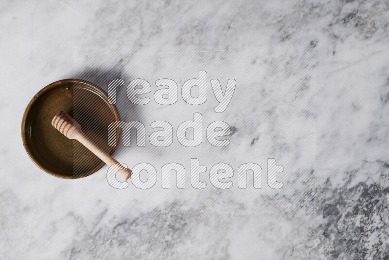 Multicolored pottery oven plate with wooden honey dipper in it on grey marble background