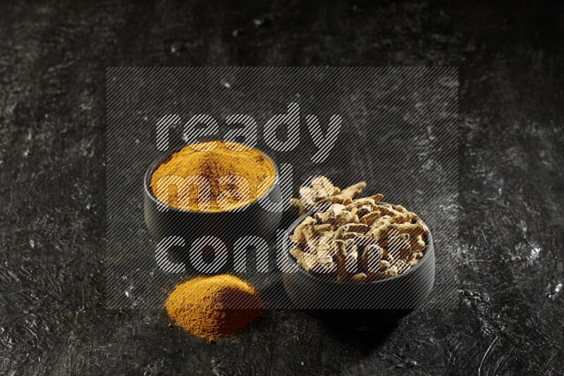 وعاءان من الفخار باللون الأسود، أحدهما ممتلئ ببودرة الكركم والآخر ممتلئ بأصابع كاملة من الكركم المجفف على خلفية سوداء