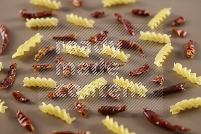 Raw pasta with different ingredients such as cherry tomatoes, garlic, onions, red chilis, black pepper, white pepper, bay laurel leaves, rosemary and cardamom on beige background