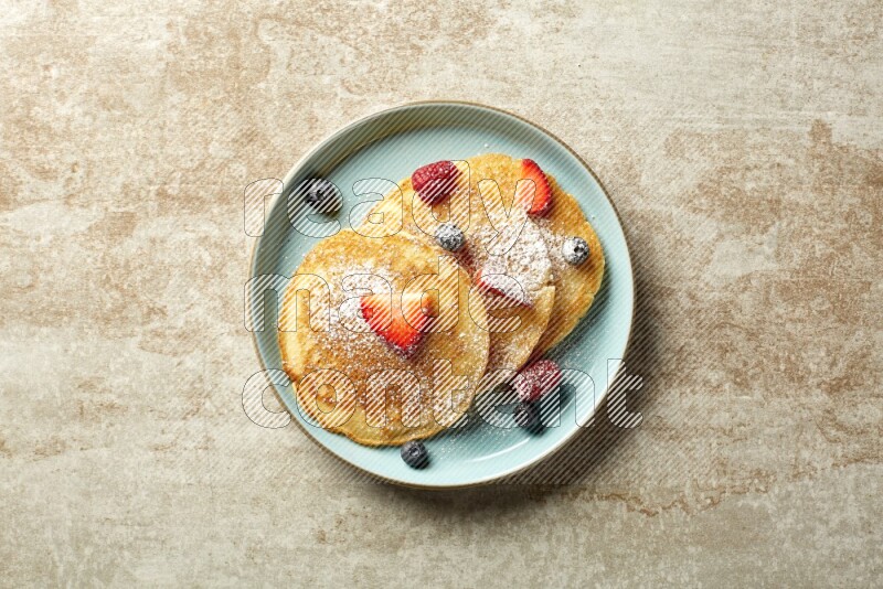 Three stacked mixed berries pancakes in a blue plate on beige background