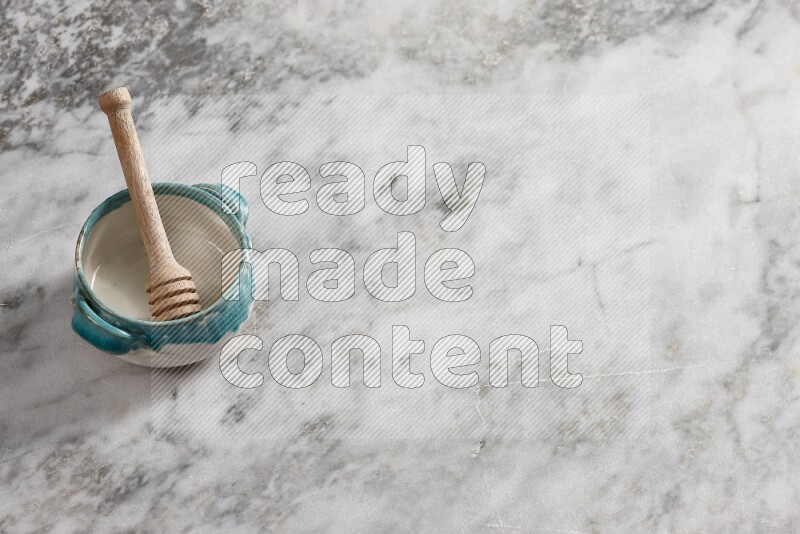 وعاء فخاري متعدد الألوان مع ملعقة عسل خشبية بداخله على خلفية من الرخام الرمادي