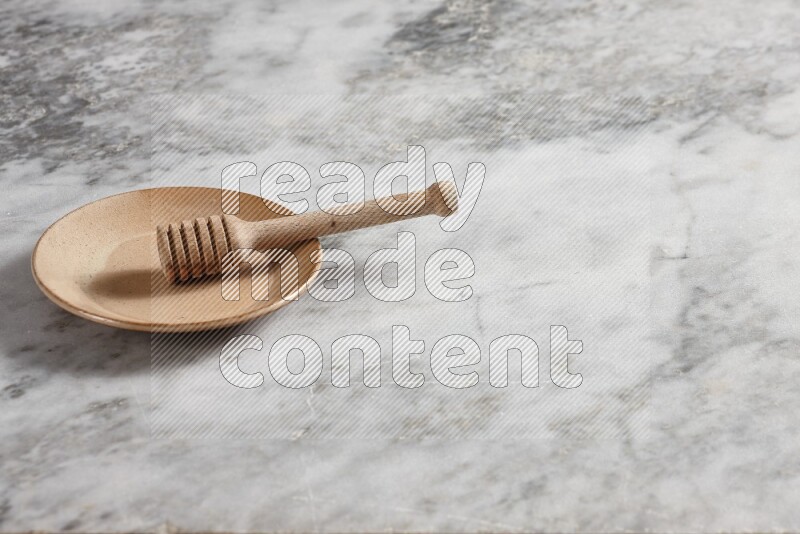 Beige pottery plate with wooden honey dipper in it on grey marble background