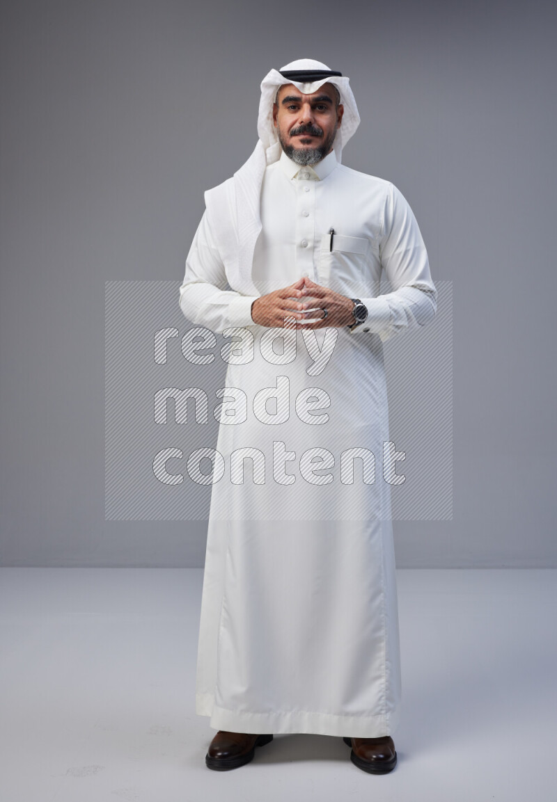 Saudi man Wearing Thob and white Shomag standing interacting with the camera on Gray background