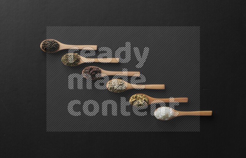 wooden spoons filled with white peppers, cloves, cardamom, salt, black peppers and basil on black flooring