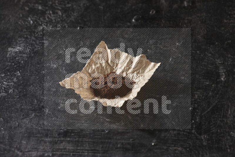 Cloves powder in crumpled piece of paper on a textured black flooring