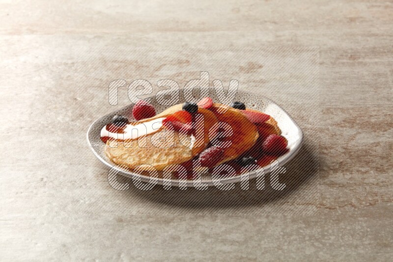 Three stacked mixed berries pancakes in an irregular plate on beige background